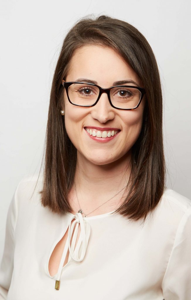 Ein Portrait einer Mitarbeiterin mit Schulterlangen braunen Haaren und schwarzer Brille.