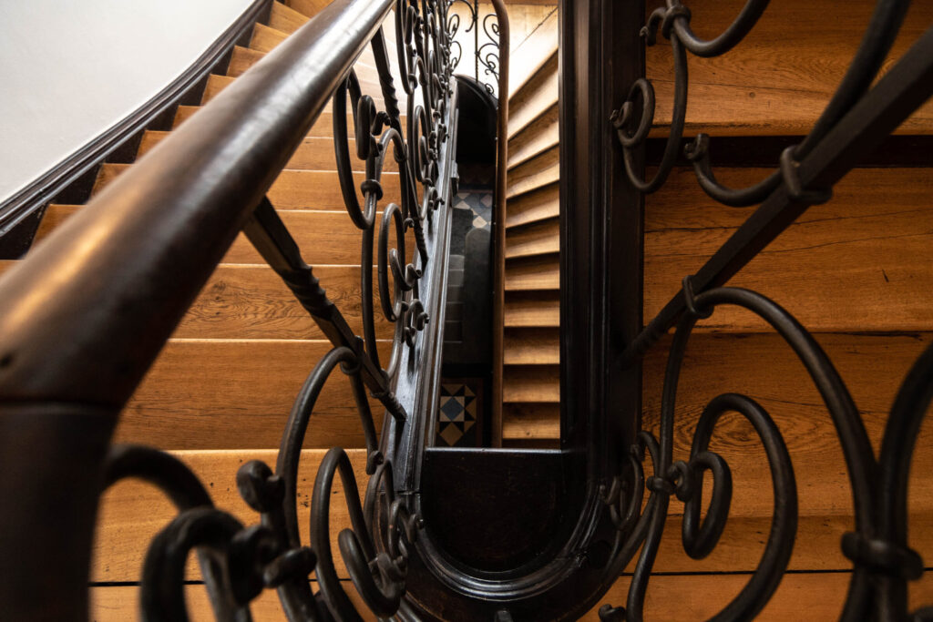 Eine Wendeltreppe von oben nach unten fotografiert mit Holzstufen und schwarzem Geländer.
